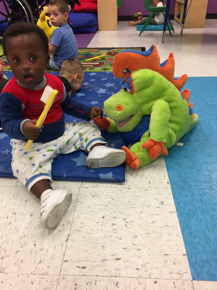 Young child playing with colorful dinosaur toy on padded floor in pediatric dental office playroom.