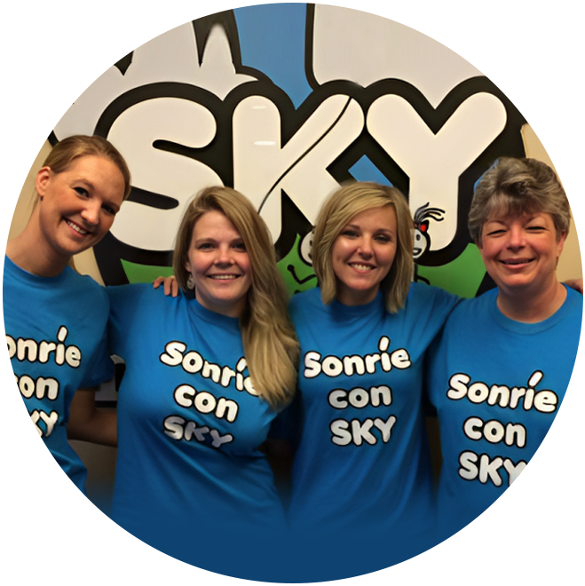 Four smiling dental team members wearing blue "Sonrie con Sky" shirts in front of branded backdrop.