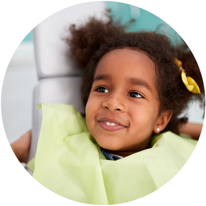 Young child smiling at camera wearing yellow-green shirt in dental office setting.