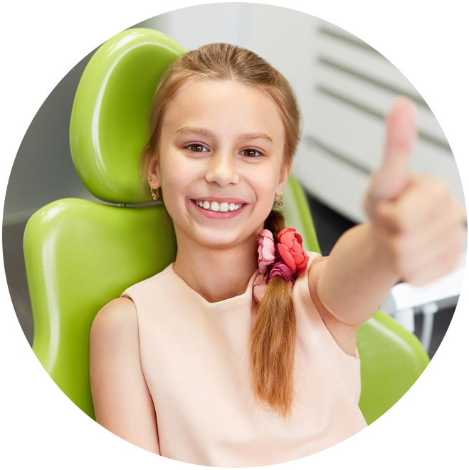 Young girl smiling and giving thumbs up in pediatric dental chair with green headrest.