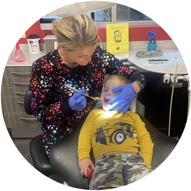 Pediatric dentist examining young child's teeth in colorful dental office setting.