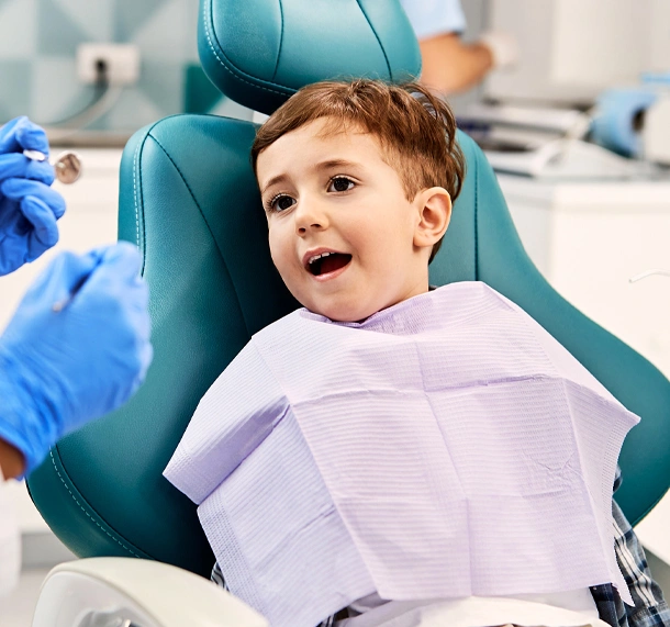 Young child in dental chair wearing protective bib during pediatric dental examination with dentist.