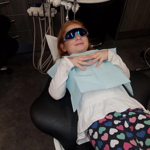 Young child wearing sunglasses reclines in dental chair during examination at pediatric dental office.