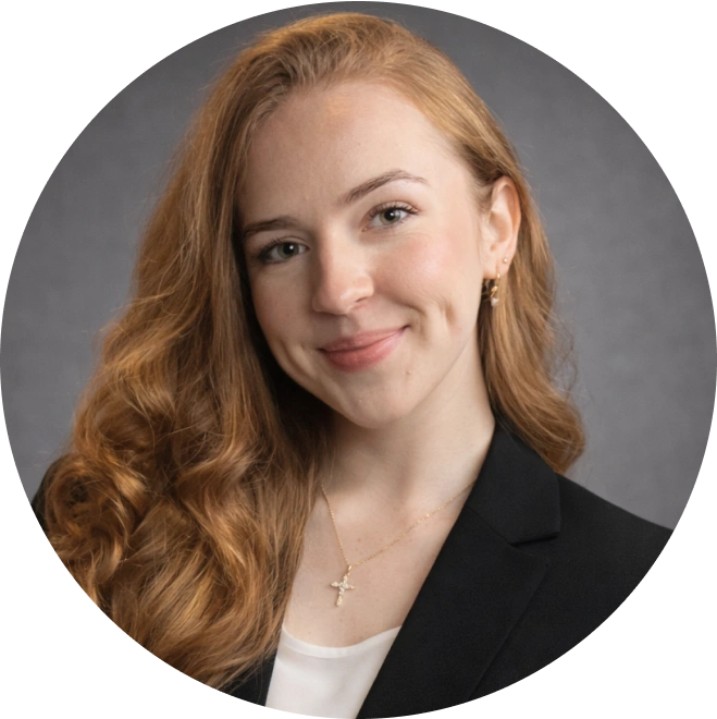 Professional headshot of a woman with reddish-brown hair wearing a black blazer against a gray background.